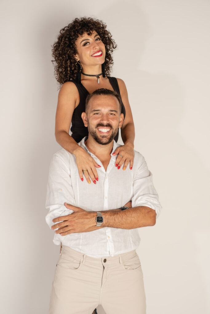 Elly y Juanma abrazados en estudio con fondo blanco, retrato de pareja de bailarines de salsa, Barcelona.