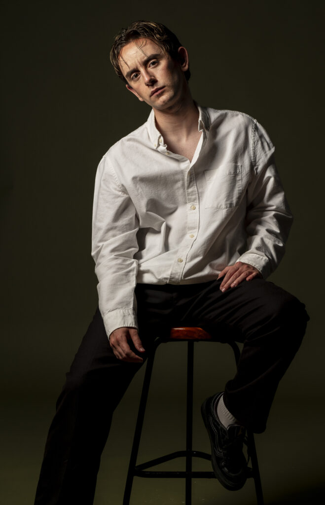 Retrato de hombre joven , mirando con expresión intensa frente a fondo oscuro.