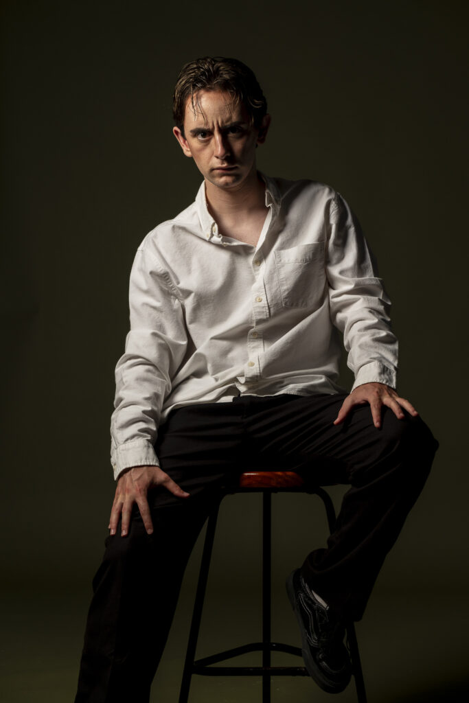 Retrato de hombre joven, mirando con expresión intensa frente a fondo oscuro.