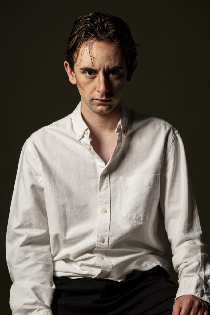 Retrato de hombre joven, mirando con expresión intensa frente a fondo oscuro.