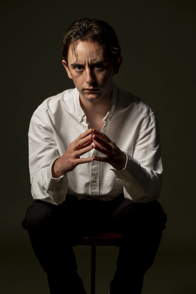 Retrato de hombre joven, mirando con expresión intensa frente a fondo oscuro.