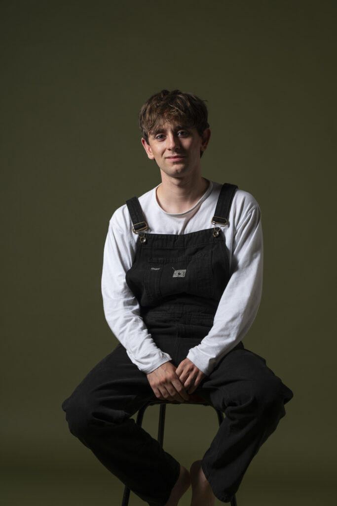 Retrato de hombre joven, mirando con expresión intensa frente a fondo oscuro.