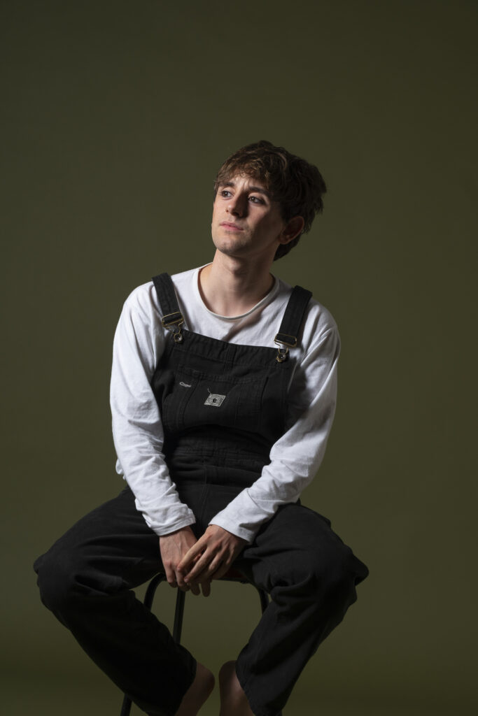 Retrato de hombre joven, mirando con expresión intensa frente a fondo oscuro.