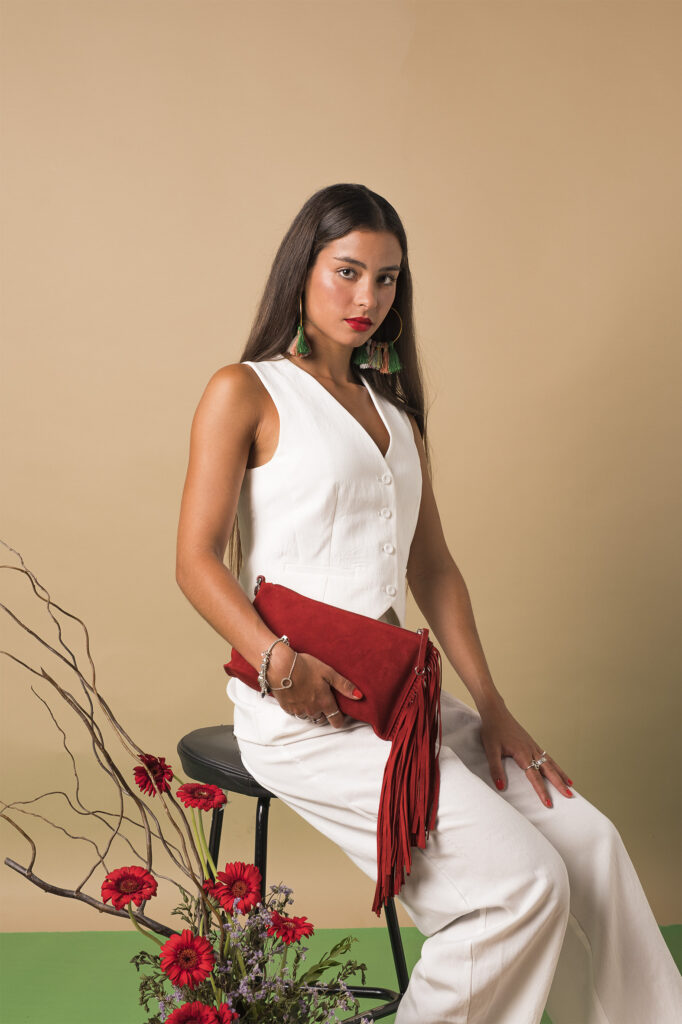 Mujer sosteniendo un bolso rojo con flecos, rodeada de pétalos de rosa y ramas decorativas.