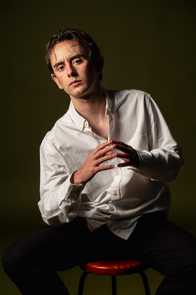 Retrato de hombre joven con barba, mirando con expresión intensa frente a fondo oscuro.